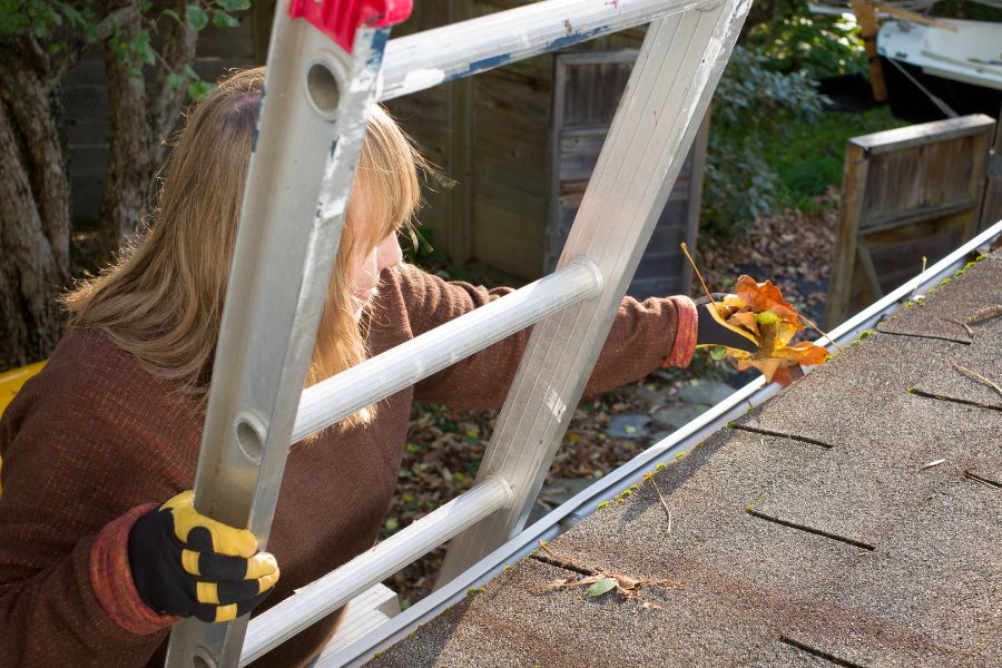 Woman homeowner cleaning eavestrough before winter 