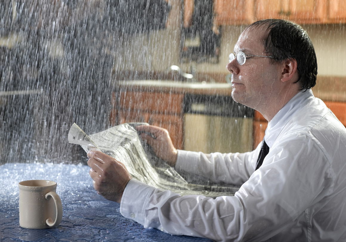 Man in suit being rained on in their house due to roof leak