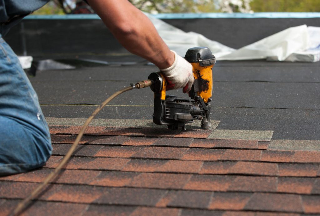 Person with nail gun installing new fiberglass shingles