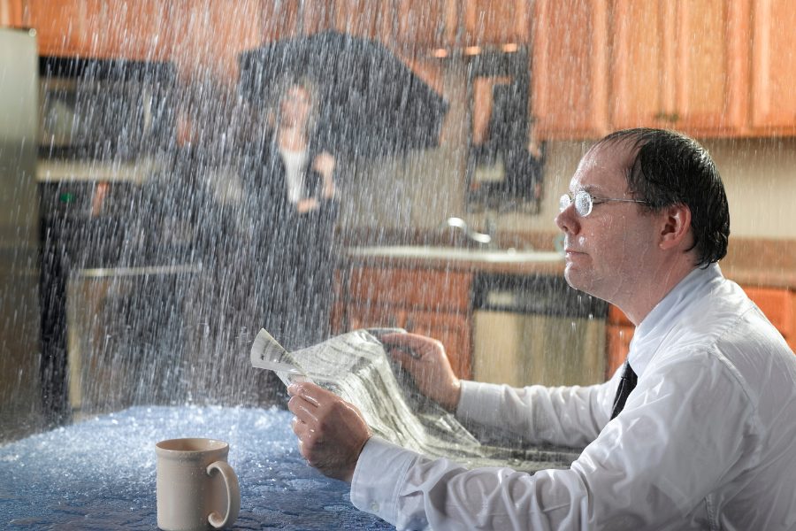 Man in home being drenched by water from leaking roof