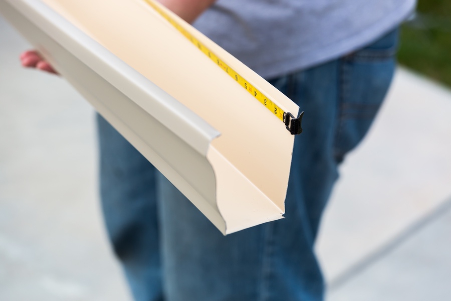 Professional holding gutter with measuring tape to ensure correct sizing for home before installation