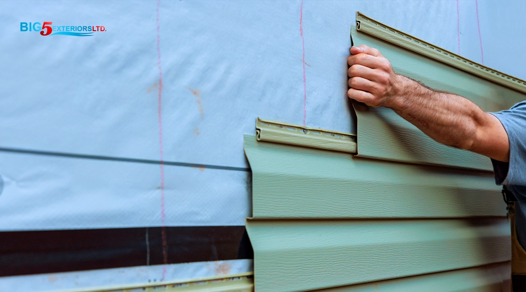 Image of worker holding up a piece of siding along side a house with a Big5 Exteriors logo in the top corner